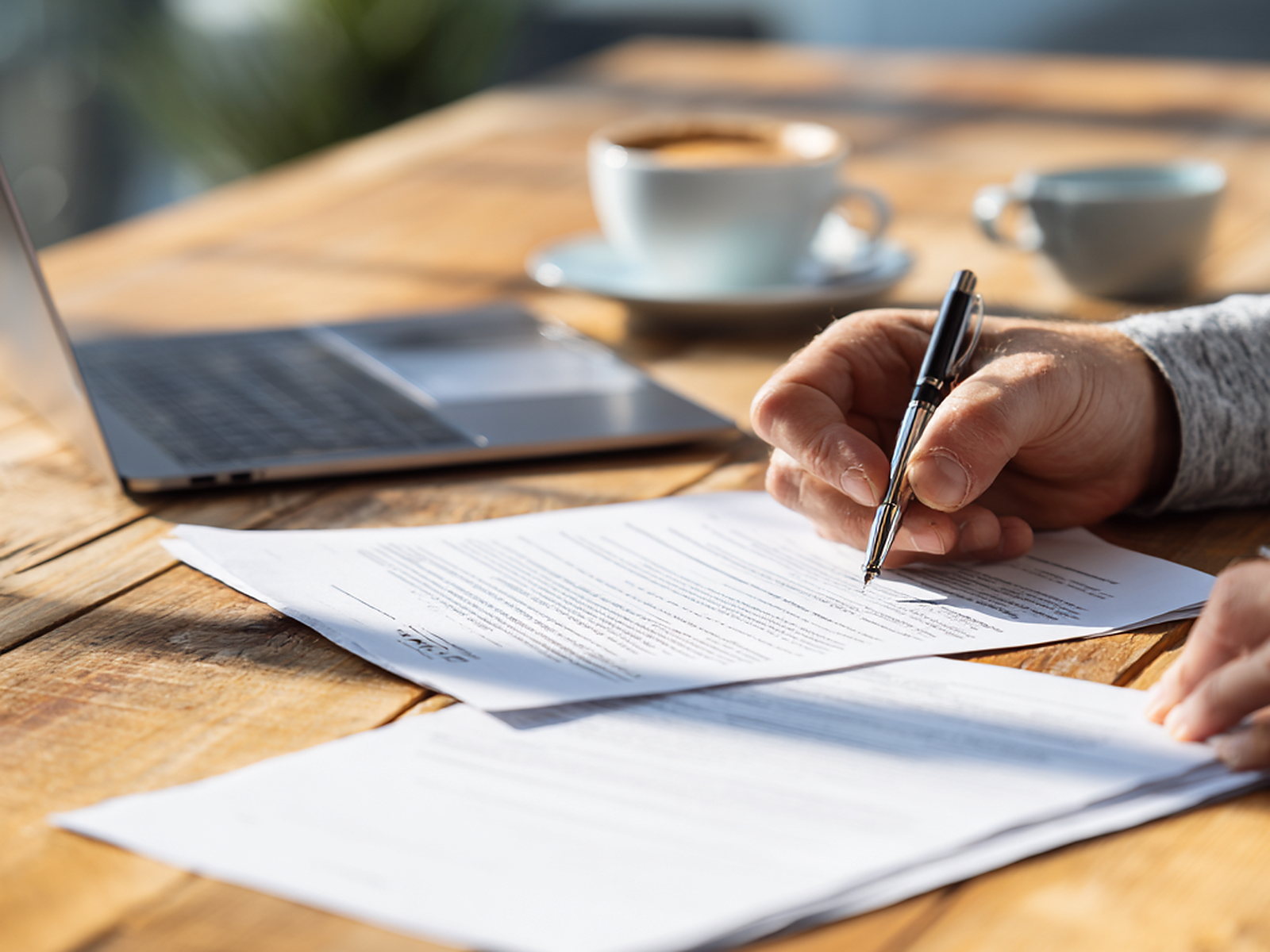 Hands using a laptop beside papers and coffee